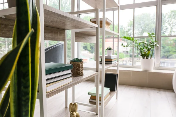 Stylish bookshelf near window in interior of modern living room