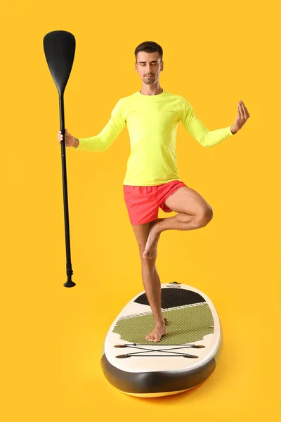 Young Man Meditating Sup Board Color Background — Stockfoto