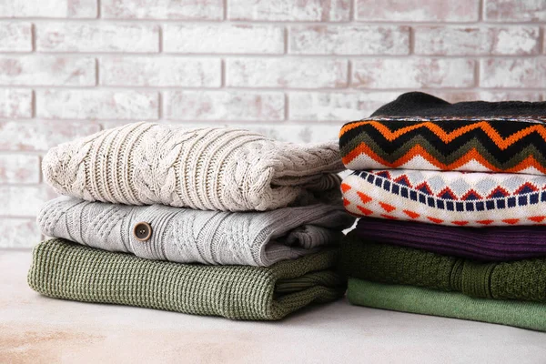 Stacks Stylish Sweaters Table Light Brick Background — Fotografia de Stock