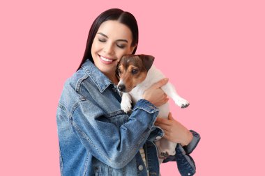 Pembe arka planda sevimli köpeği olan mutlu genç bir kadın.