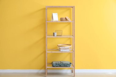 Çerçeveli, sepetli ve ekoseli ahşap raf ünitesi sarı duvarın yanında.