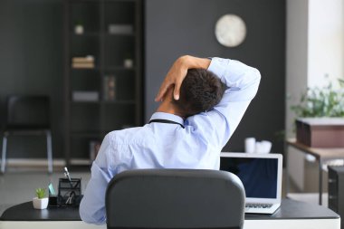 Genç işadamı ofiste çalışırken omurgasını esnetiyor.