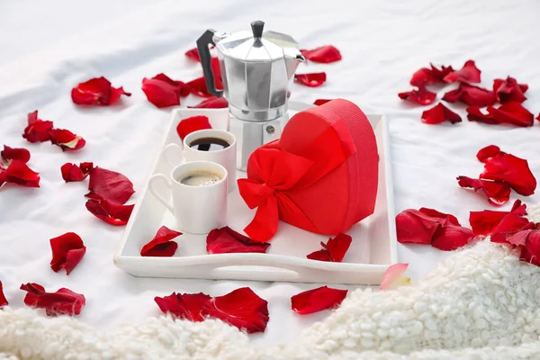 バレンタインデーの贈り物と赤いバラの花びらで覆われたベッドの上のコーヒーとトレイ — ストック写真