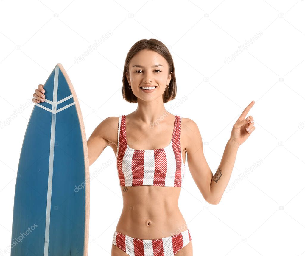 Beautiful young woman with surfboard pointing at something on white background