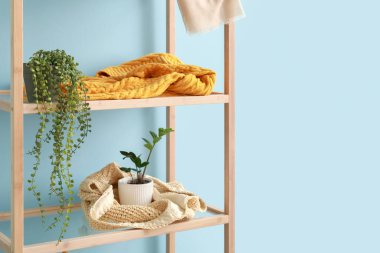 Mavi duvarın yanında saksıları olan ahşap raf ünitesi.