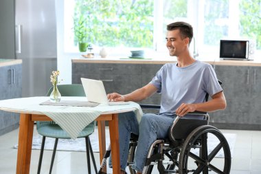 Mutfakta dizüstü bilgisayar kullanan fiziksel engelli bir genç.
