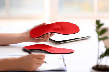 Kırmızı ortopedik taban tutan ve masada not alan kadın hemşire, yakın plan.