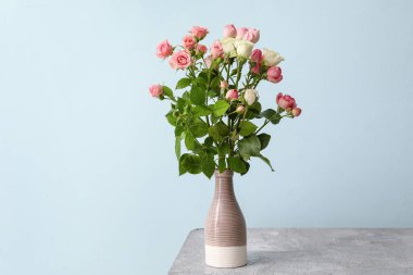 Masanın üzerinde bir buket gül olan vazo.