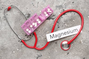 İçinde haplar, steteskop ve grunge arkaplanda kelime MAGNESIUM olan plastik bir kap.