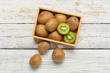 Açık ahşap arka planda taze olgun kivi dolu bir kutu.