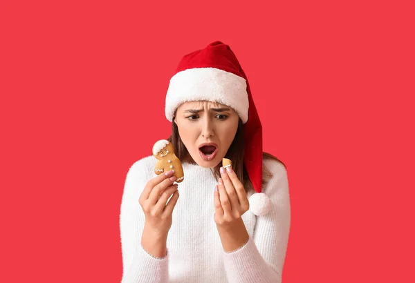 Shocked Young Woman Santa Hat Broken Gingerbread Cookie Red Background — Stock Photo, Image