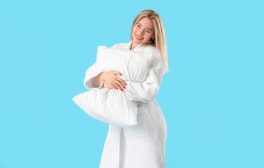 Bornozlu genç bir kadın mavi arka planda yastığa sarılıyor.