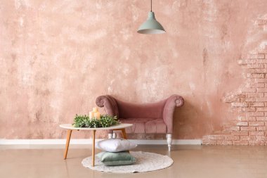 Çelenkli masa, mumlar, yastıklar ve pembe duvarın yanındaki şık koltuk.