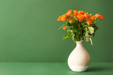 Yeşil arka planda güzel turuncu gülleri olan vazo