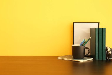 Renkli duvarın yanındaki masada kalem ve kitaplarla dolu bir kupa.