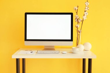 Modern bilgisayarlı işyeri, bir fincan kahve ve renkli duvarın yanında pamuk çiçekler.