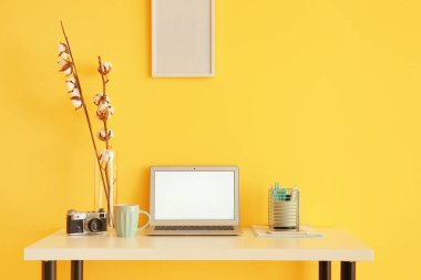 Modern dizüstü bilgisayar, cep telefonu ve renkli duvarın yanındaki masada klasik fotoğraf makinesi.