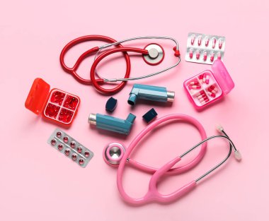 Astım spreyleri, steteskoplar ve pembe arka planda haplar.