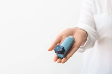 Işık arka planında astım spreyi tutan kadın.