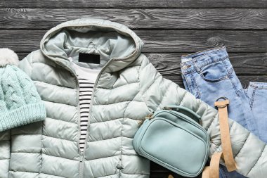 Siyah ahşap arka planda şık bir ceket, şapka, çanta ve kot.