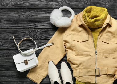 Şık ceket, kulaklık, çanta, ayakkabı ve kemer siyah ahşap arka planda.