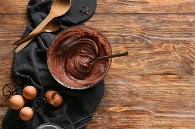 Tahta arka planda çikolatalı kek hazırlamak için taze hamurlu ve yumurtalı kase.