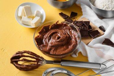 Sarı arka planda çikolatalı kek hazırlamak için taze hamur ve malzemelerle dolu bir kase.