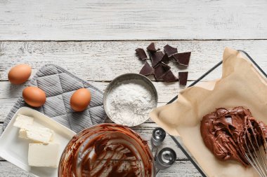 Beyaz ahşap arka planda çikolatalı brownie hazırlamak için taze hamur ve malzeme içeren fırın tabağı.