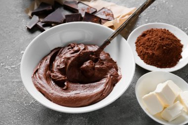 Gri arka planda çikolatalı kek hazırlamak için taze hamur ve malzemelerle dolu bir kase.
