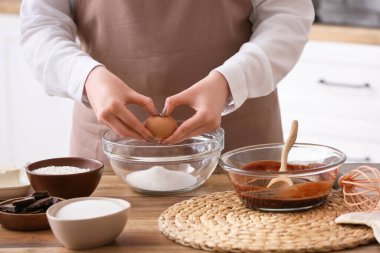 Mutfakta çikolatalı kek hazırlayan kadın kaseye yumurta ekliyor.