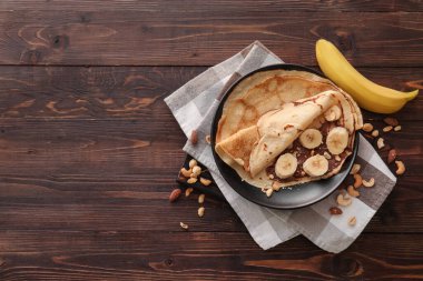 Çikolata ezmeli, fındıklı ve ahşap zemin üzerinde muz dilimlenmiş leziz ince krepler.