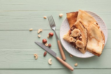 Çikolata ezmeli, muzlu ve fındıklı, yeşil ahşap arka planda lezzetli, ince krepler.