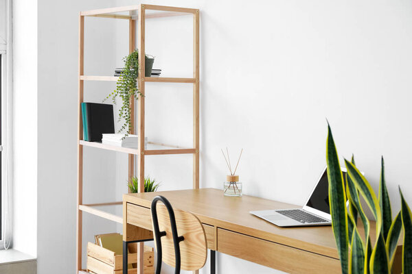 Modern workplace with laptop and shelving unit near light wall