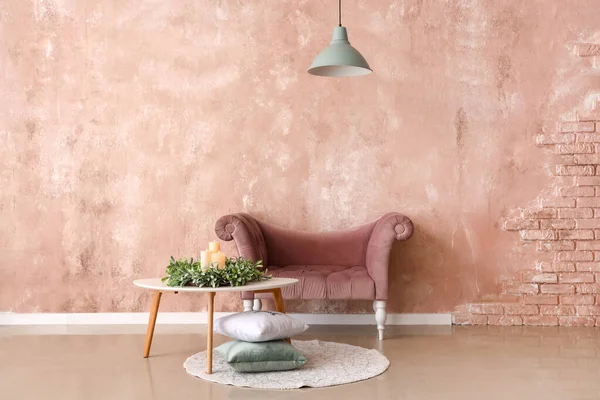 Çelenkli masa, mumlar, yastıklar ve pembe duvarın yanındaki şık koltuk.