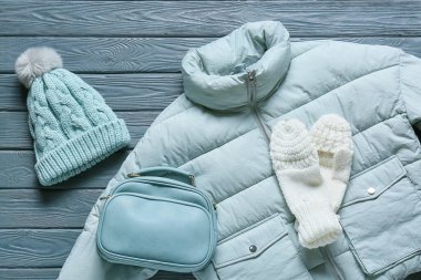 Stylish female jacket, hat, bag and mittens on grey wooden background