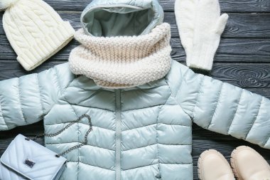 Stylish jacket, hat, bag and mittens on black wooden background