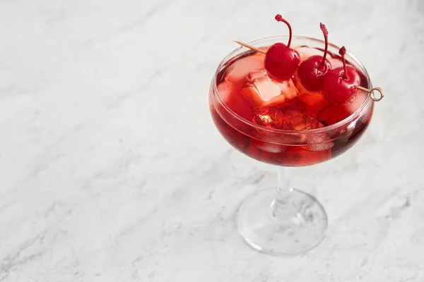 Glass of iced Manhattan cocktail with cherries on light background, closeup