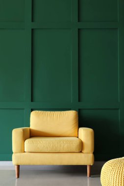 Yeşil duvarın yanında rahat sarı koltuk ve puf