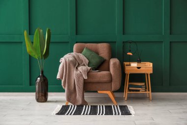 Koltuğu, masası ve vazosu olan bir oda. Palmiye yaprakları renkli duvarın yanında.