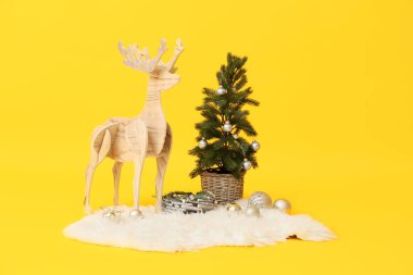 Sarı arka planda Noel ağacı olan tahta ren geyiği.