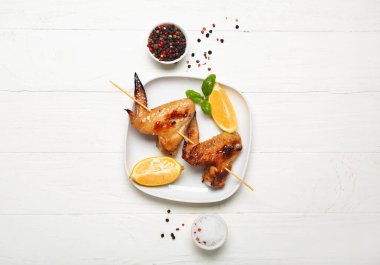 Izgara tavuk kanatlı tabak şiş ve beyaz ahşap arka planda limon.