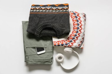 Erkek kazakları, pantolonları, cep telefonu ve kulaklıkları açık arkaplanda.