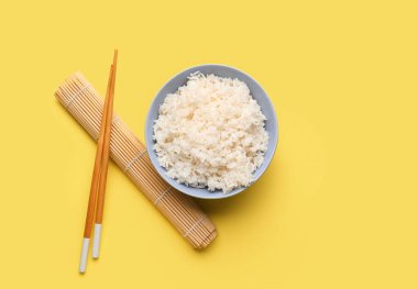 Lezzetli haşlanmış pirinç, yemek çubukları ve sarı arka planda paspas.