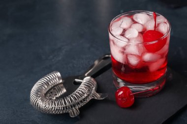 Bir bardak Manhattan kokteyli ve siyah arka planda süzgeç.