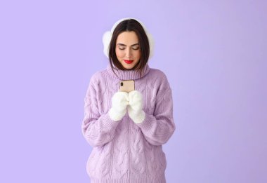 Kalın süveterli ve telefonlu genç bir kadın.