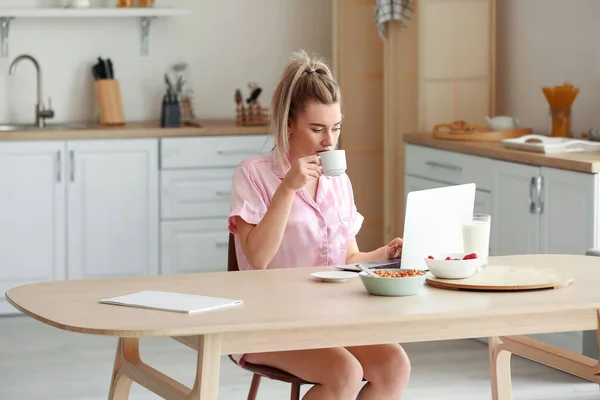 Güzel Genç Bayan Mutfakta Dizüstü Bilgisayar Kullanırken Kahve Içiyor — Stok fotoğraf