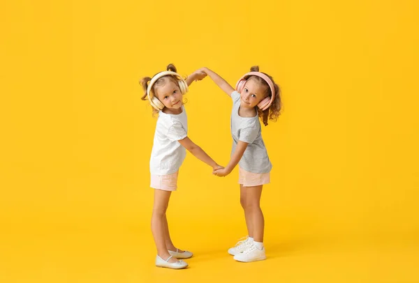 Χαριτωμένα Κοριτσάκια Ακουστικά Που Κρατιούνται Χέρι Χέρι Κίτρινο Φόντο — Φωτογραφία Αρχείου