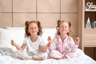 Yatak odasında meditasyon yapan sevimli küçük kızlar.