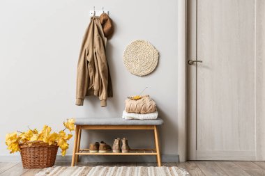 Ceket ve şapka ışık duvarında ve sepetinde asılı. Sonbahar yaprakları şık koridorun içinde.