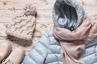 Kışlık ceket, atkı, şapka ve ayakkabı açık ahşap arka planda.